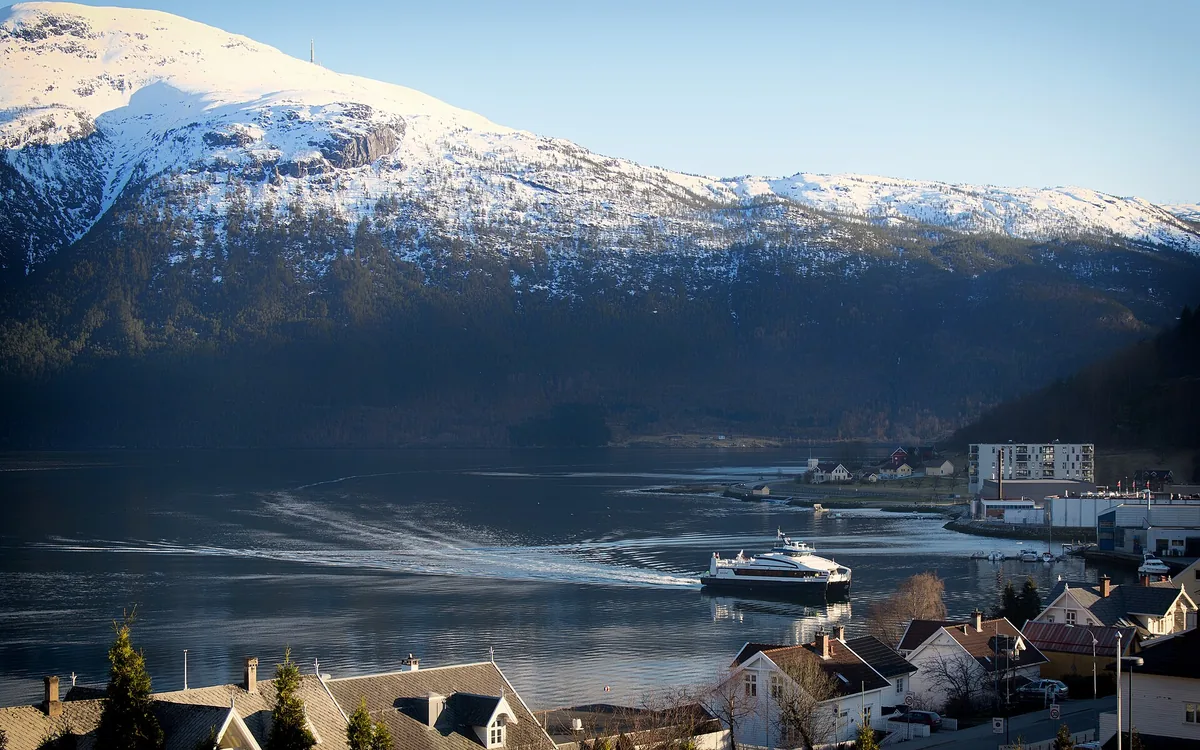 Snødekte fjell over Sogndalsfjorden, med båt og hus langs fjorden